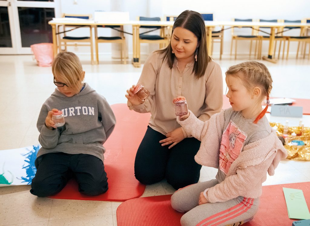 Kuvassa keskellä lastentunnetaito-ohjaaja Pia Ilves sekä hänen vierellään ryhmään osallistuneet Toivo ja Venla. Kolmikko tutkailee tekemiään huminapurkkeja.